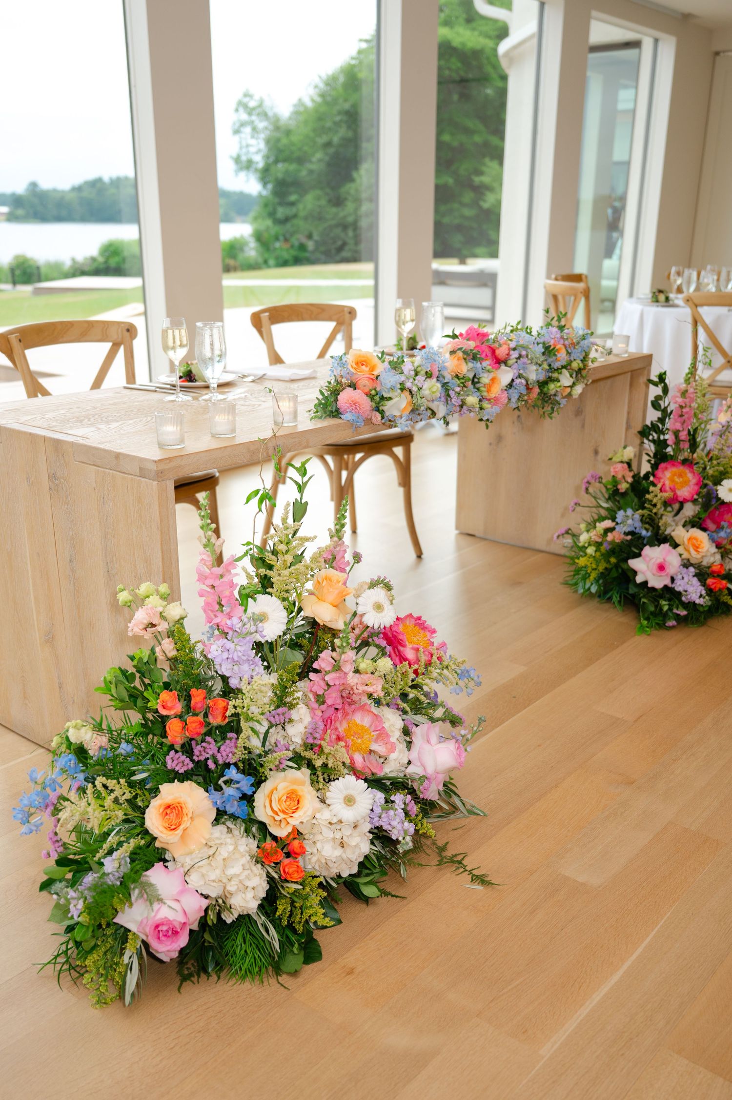 Colorful floral arrangements with pink, orange, and blue blooms line a light wooden table elegantly at the Lakehouse in Halifax, MA