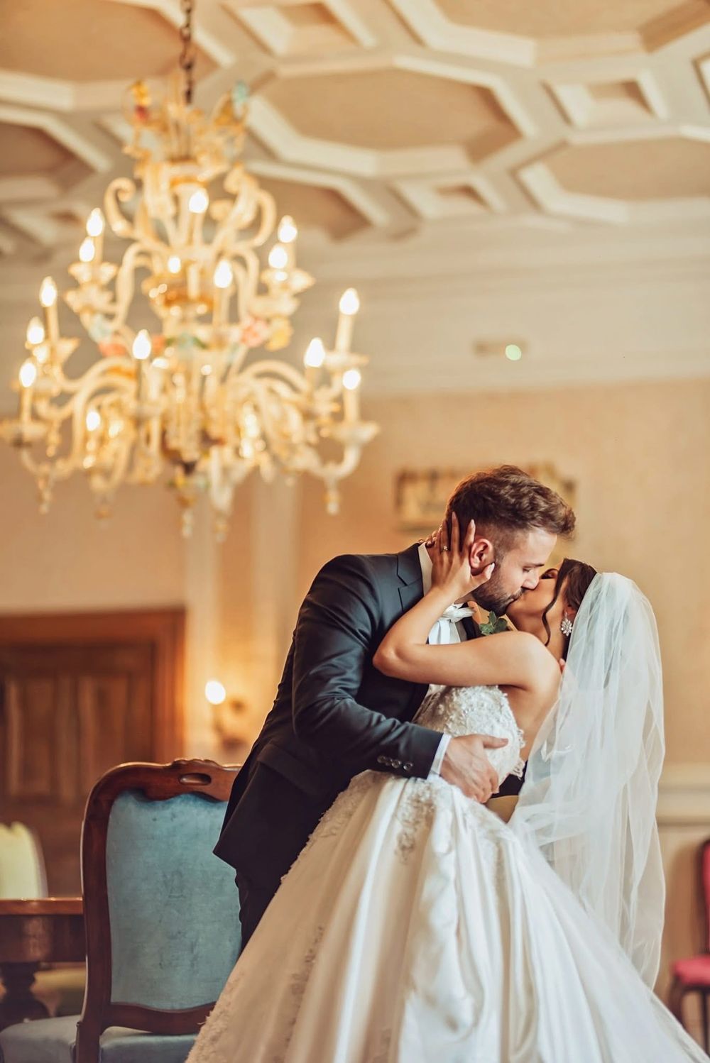 Elegant wedding scene with crystal chandeliers as a couple in formal attire share an intimate moment in a grand ballroom.