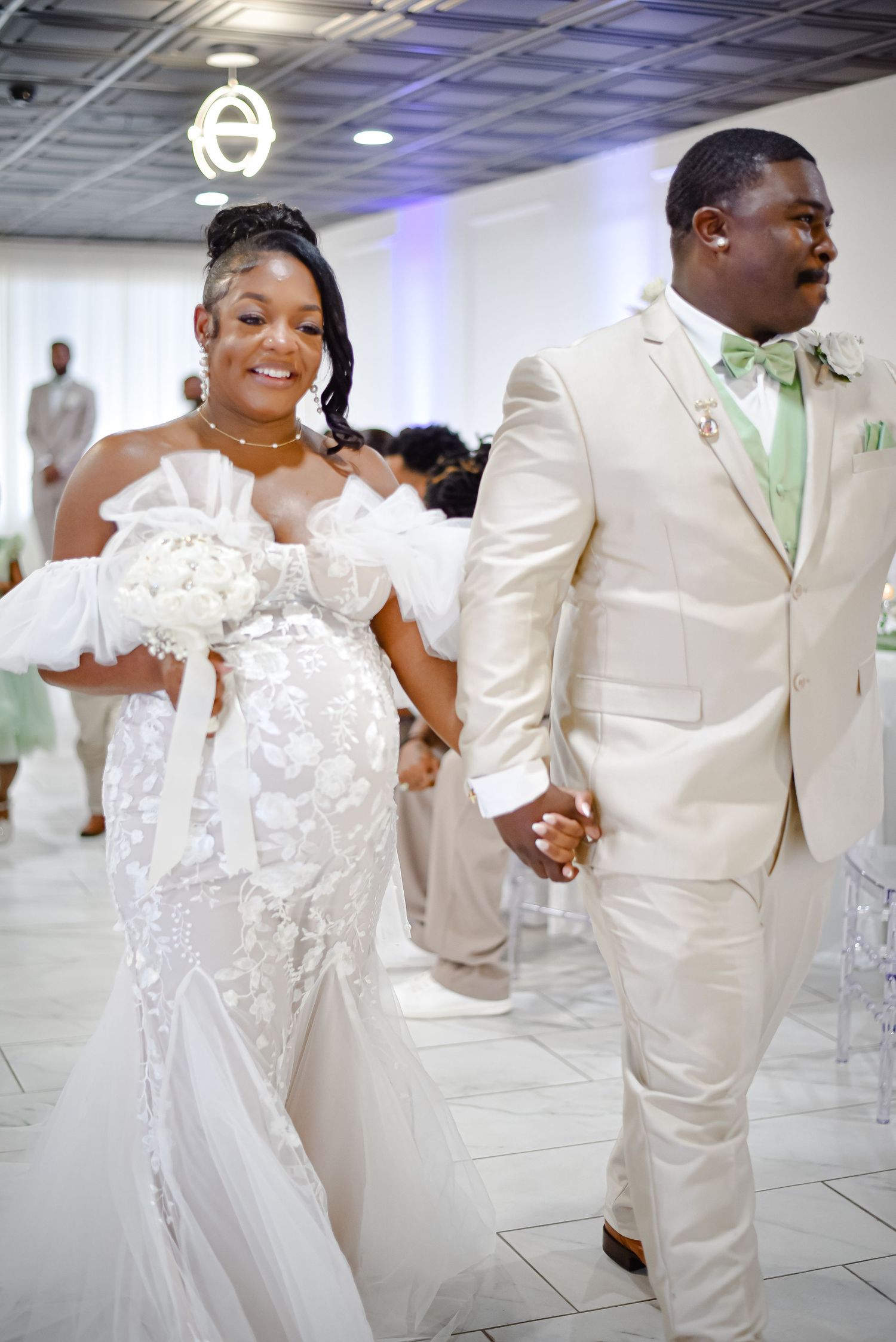 Wedding couple in elegant white attire holding hands during their ceremony.