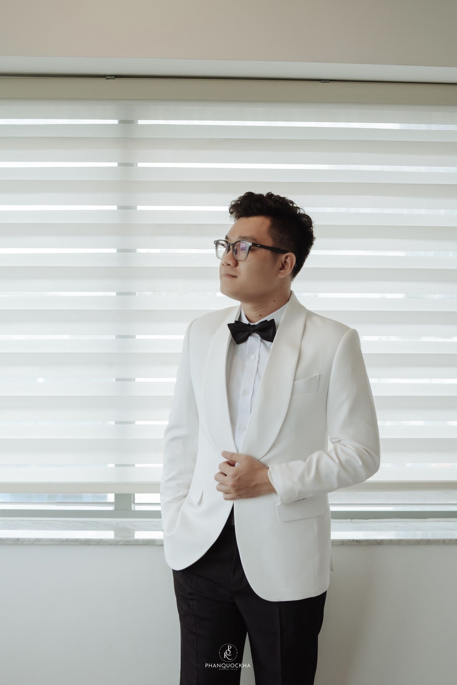 Groom in white tuxedo jacket and black bow tie adjusting his suit before wedding ceremony.