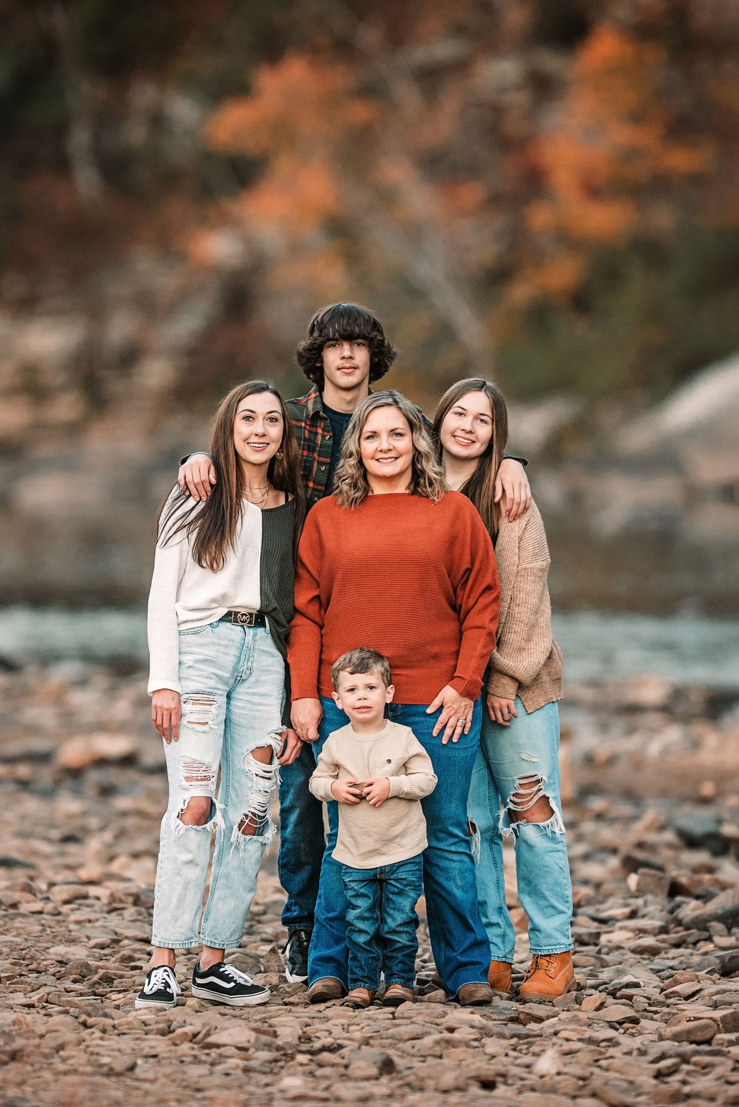 A family of five poses together on a rocky riverbank surrounded by autumn foliage and flowing water.