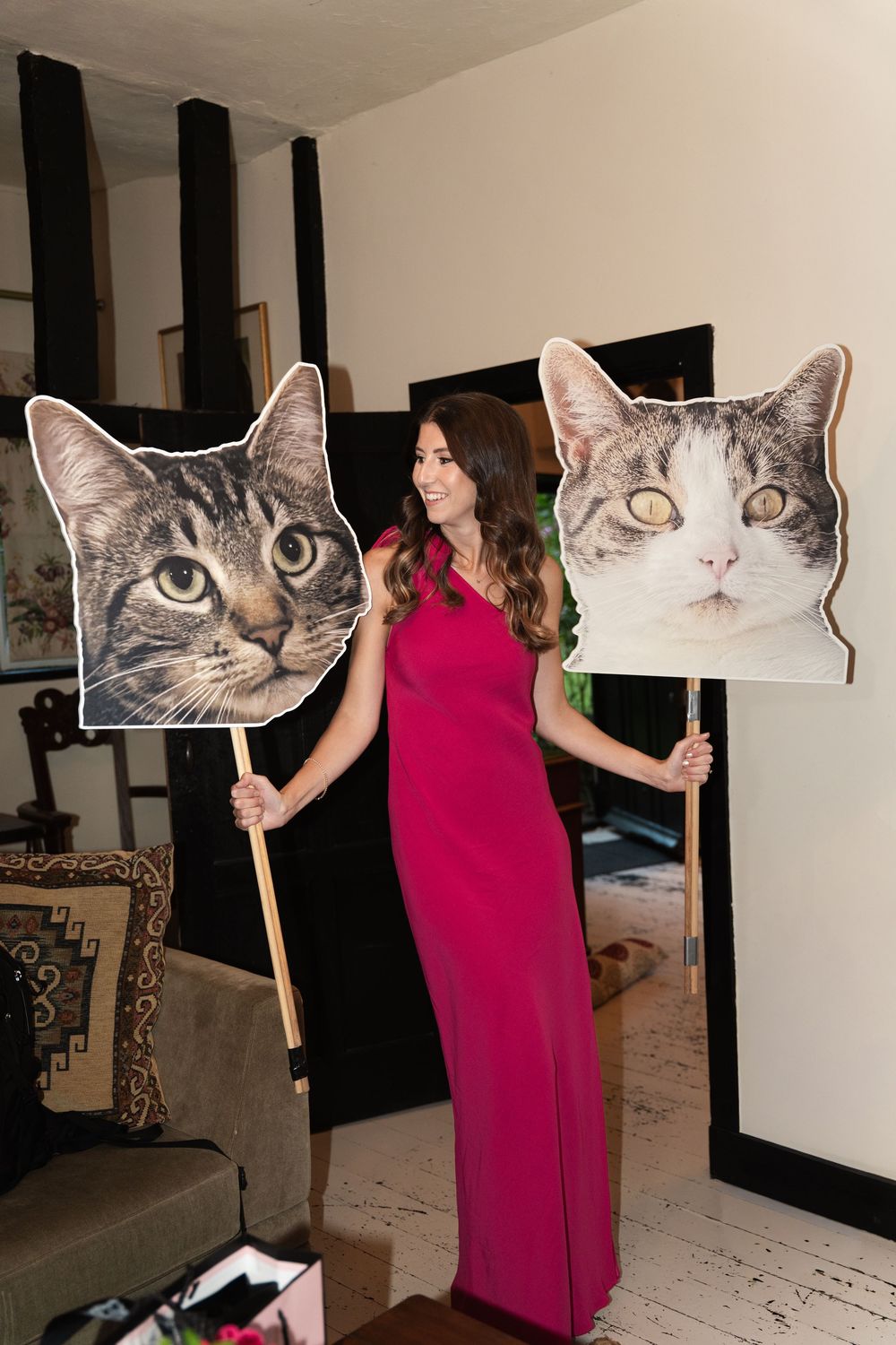 A sequence of photos showing someone in a pink dress manipulating large cat face cutouts on sticks against a white wall.