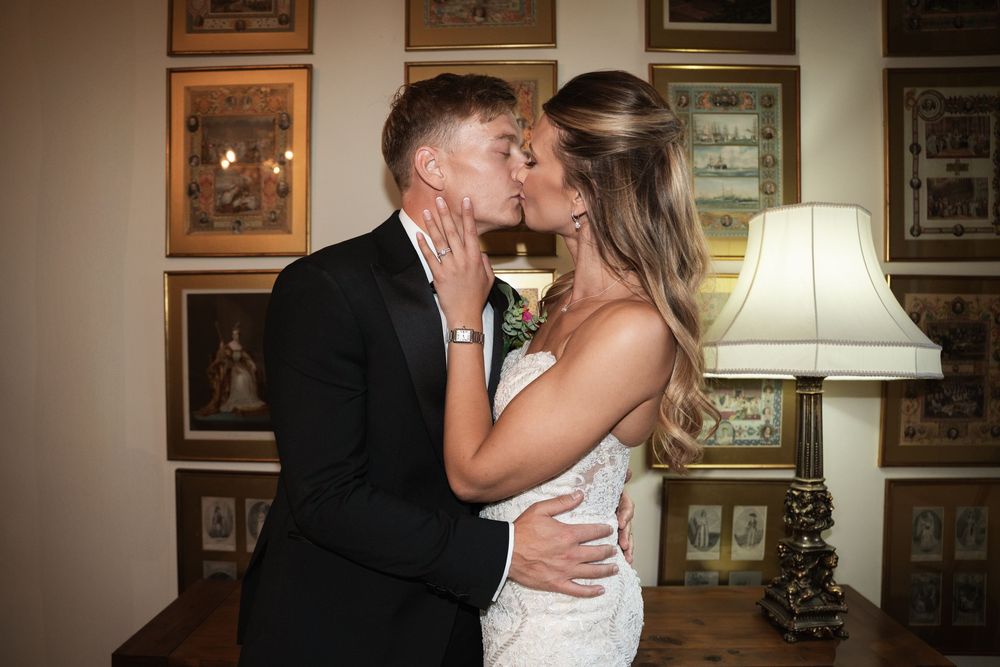 A couple in formal wedding attire sharing romantic kisses in sequence against a wall with framed artwork.
