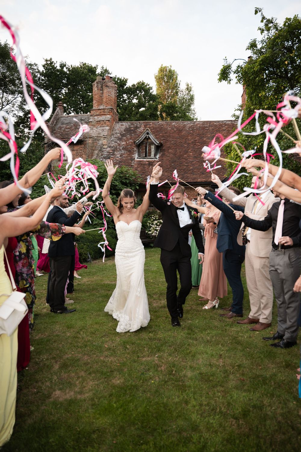 Wedding attendees form a grand tunnel while waving pink and white ribbon wands for celebratory exit.