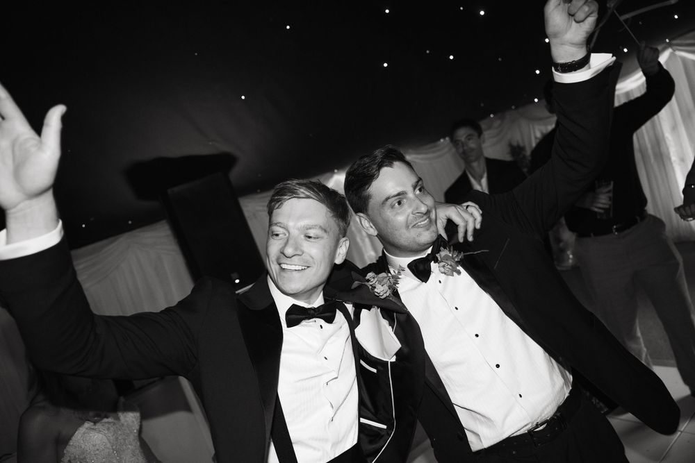 Black and white image showing a group of dapper people in tuxedos socializing at a formal event.