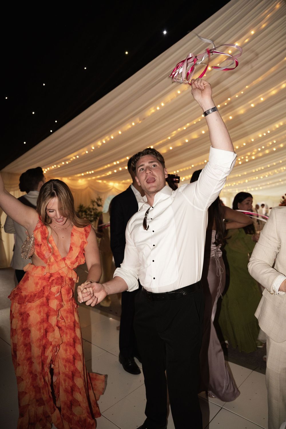 People dancing together in a wedding reception tent illuminated by romantic string lights and glowing decor.