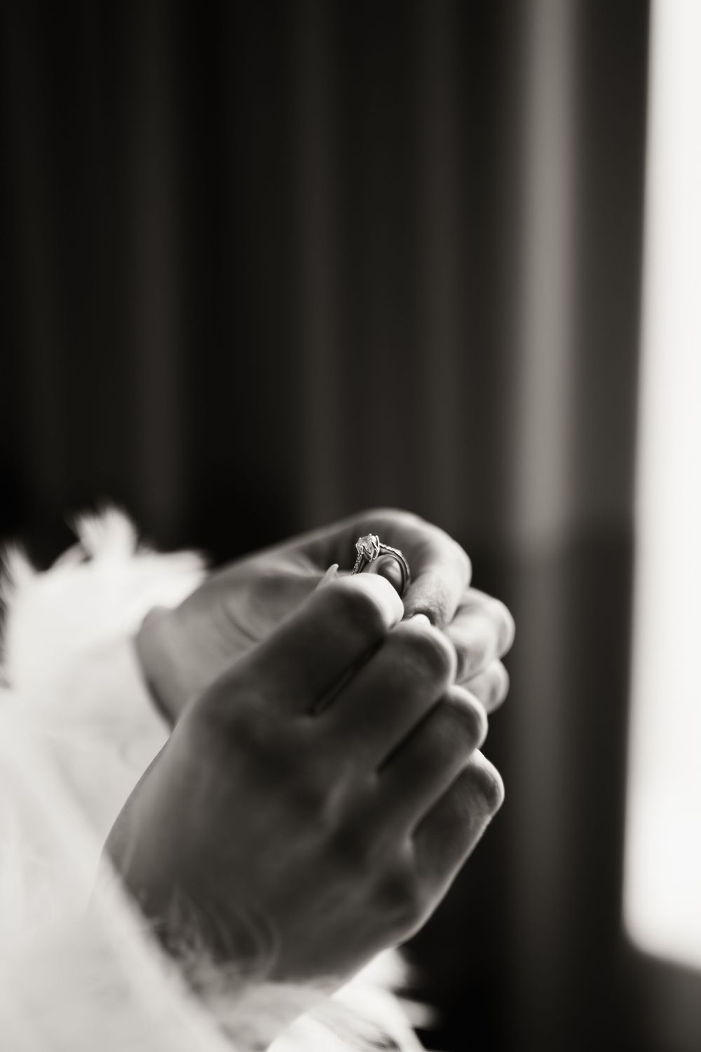A black and white close-up photo of hands holding a small ring in soft lighting with a dark background.
