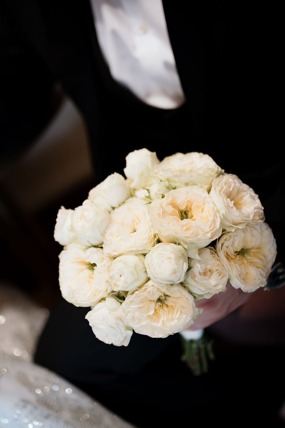 A delicate bouquet of cream-colored garden roses arranged in a classic round bridal style against a dark background.