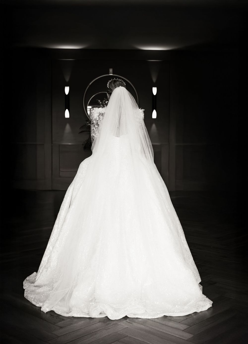 A dramatic black and white photo of a wedding dress displayed from behind showing its full ball gown silhouette and veil.