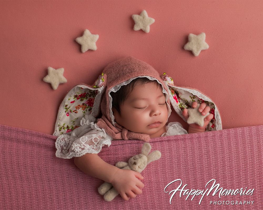 Sleeping newborn surrounded by star decorations on pink backdrop.