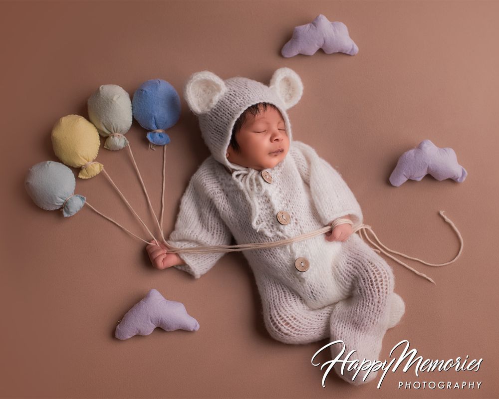 Sleeping newborn with soft toys and clouds in artistic studio setup.