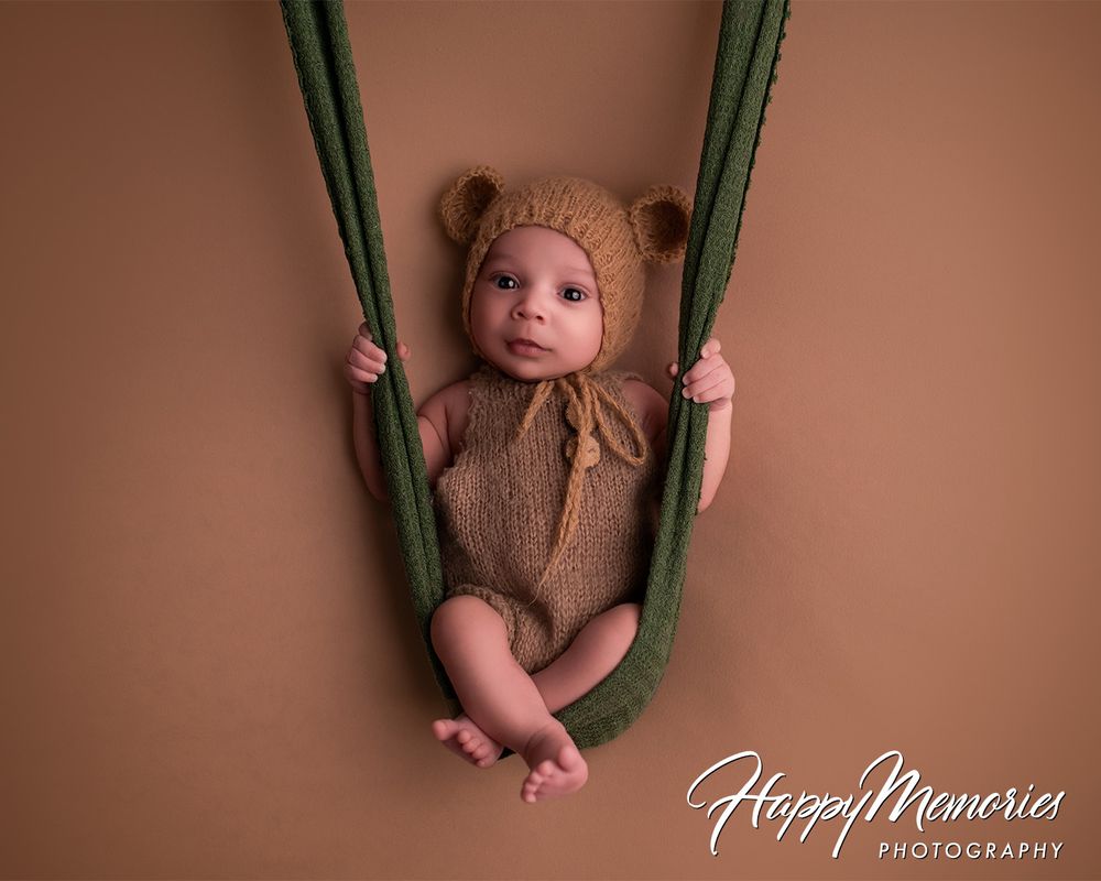 Newborn sleeping in miniature green swing against neutral background.