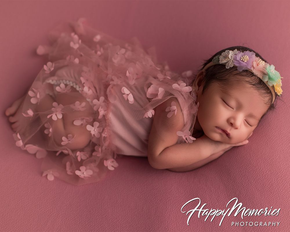 Dreamy newborn portrait on pink background with delicate floral accents.