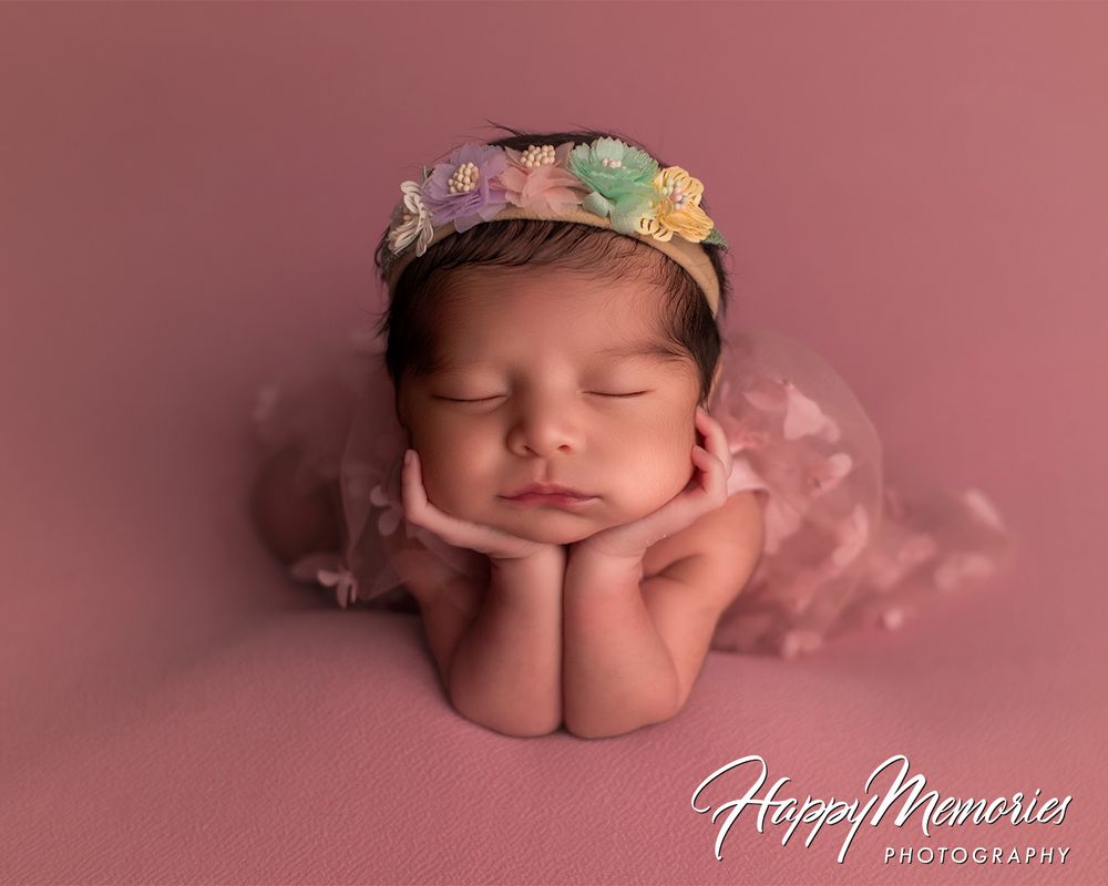 Artistic newborn photo with soft pink tones and floral headpiece.