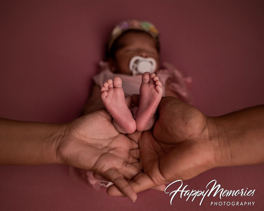 Close-up of tiny newborn feet and hands against coral background.