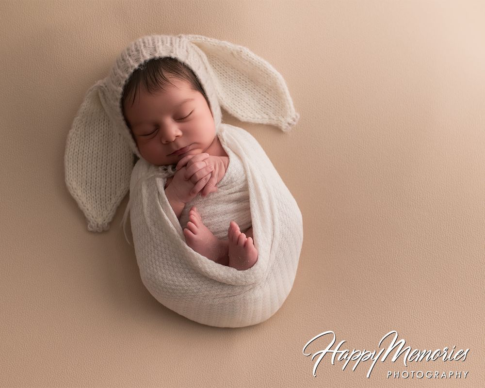 Serene newborn portrait wrapped in white knit blanket on neutral background.