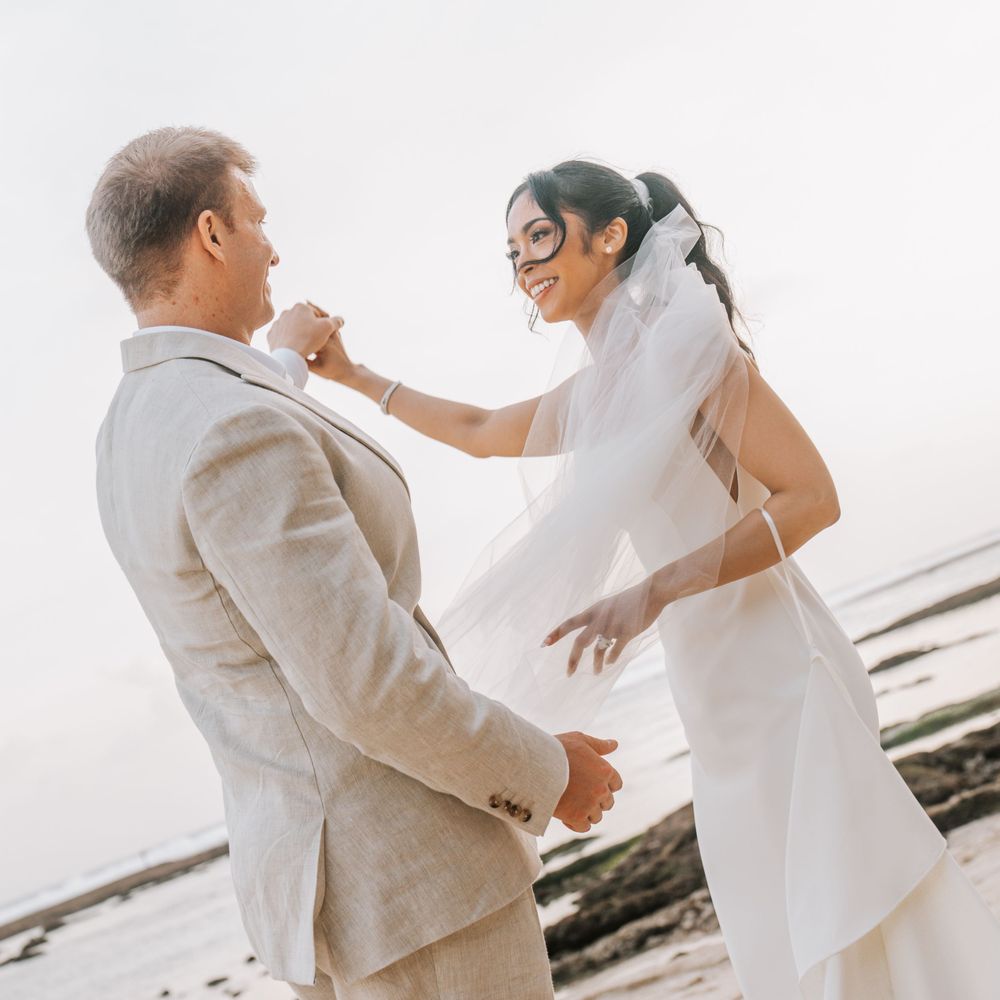 Couple in wedding attire sharing romantic dance moves on a sunlit beach during their celebration.