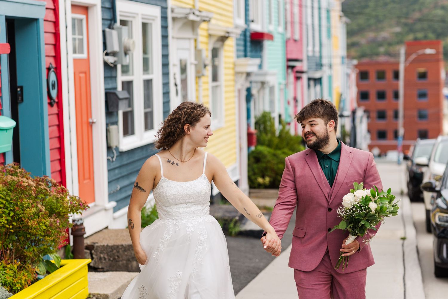 A couple walks and stands together on a colorful street lined with brightly painted houses and balconies.