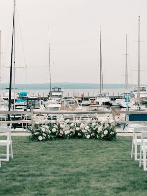 Outdoor wedding ceremony setup with white chairs and floral arrangements overlooking a marina filled with sailboats.