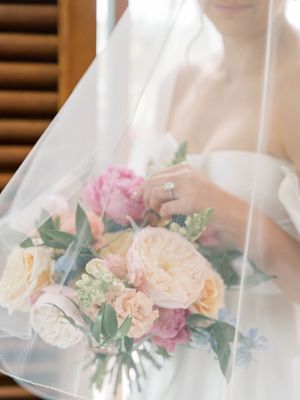 Delicate floral bouquet with pink and cream roses behind sheer white wedding veil fabric.