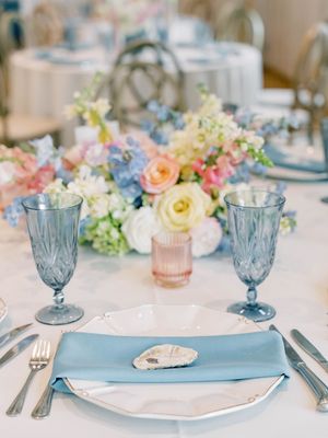 Elegant table setting with blue goblets, white plates and pastel floral arrangements.