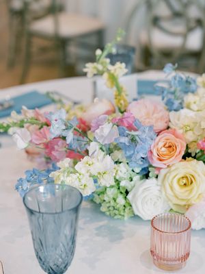 Wedding reception table setting with blue glassware and pastel floral centerpieces.