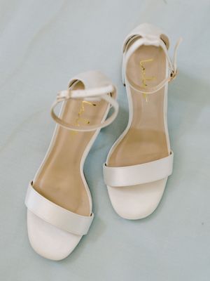 White bridal sandals with ankle straps on light blue background.