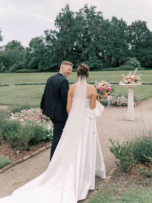 Wedding couple walking along garden path with floral arrangements and outdoor decor.