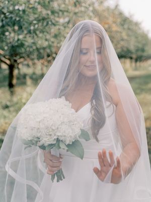 Ethereal bridal portraits with white flowers and flowing veil in an orchard setting.