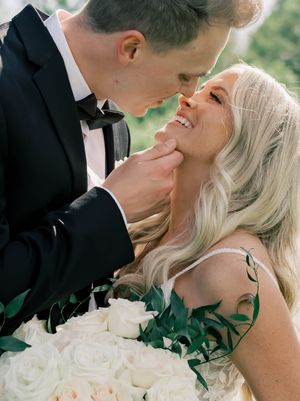 Romantic wedding couple sharing intimate moments with white roses in an outdoor setting.