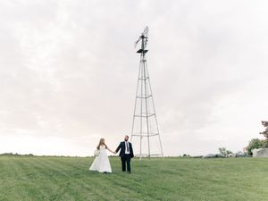 Wedding couple silhouetted against cloudy sky with windmill in background.