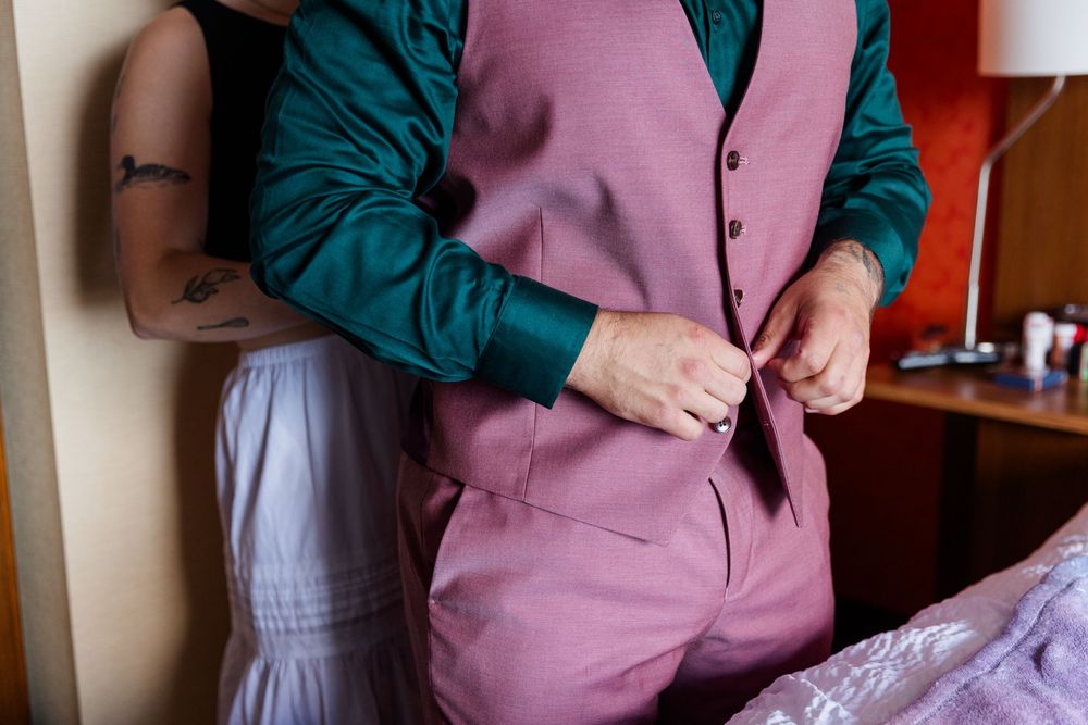 Someone buttoning up a stylish pink vest over a teal green shirt.
