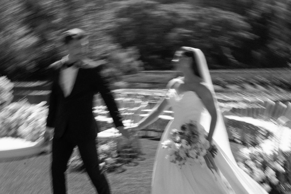 Black and white motion blur photo of bride and groom holding hands at outdoor wedding.