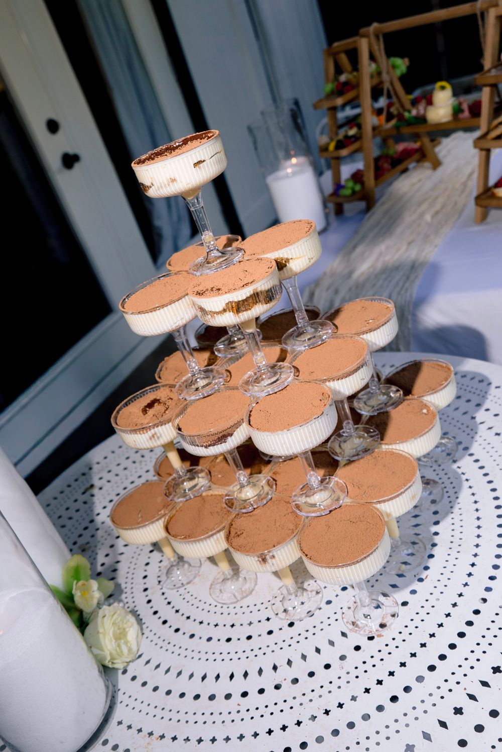Elegant tiramisu dessert tower display with layered cups on a decorative white lace tablecloth at a wedding reception.