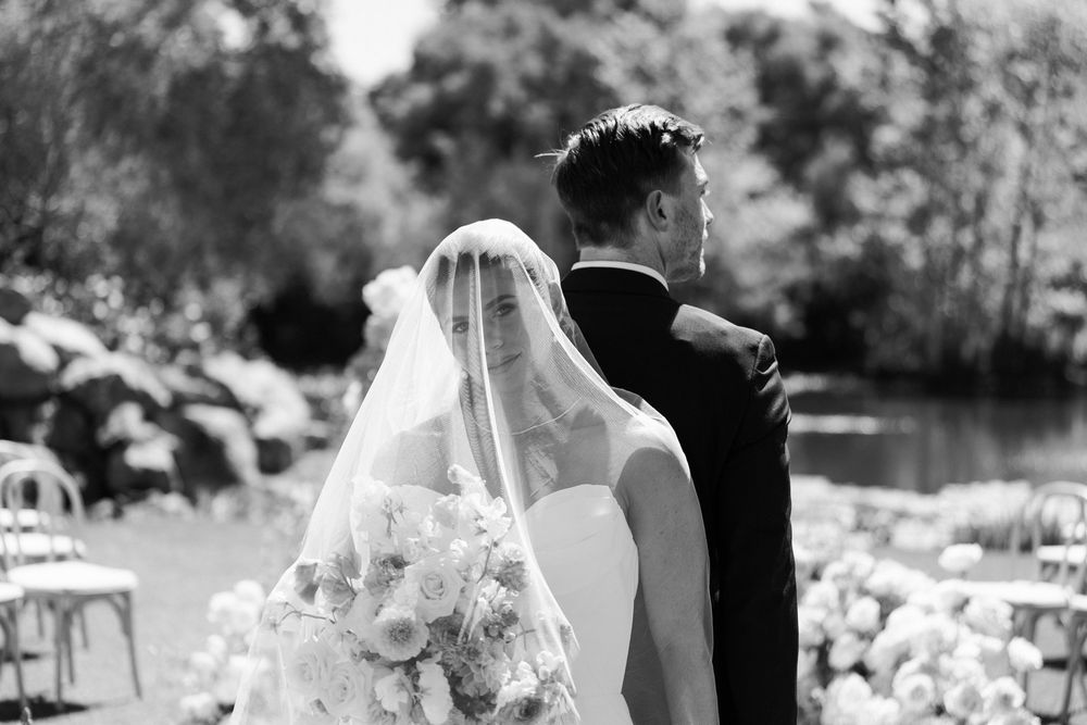 Black and white photo of bride and groom standing together at floral outdoor wedding ceremony.