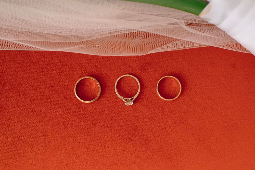 Three gold wedding rings including a diamond engagement ring displayed on a red velvet surface with a white veil.