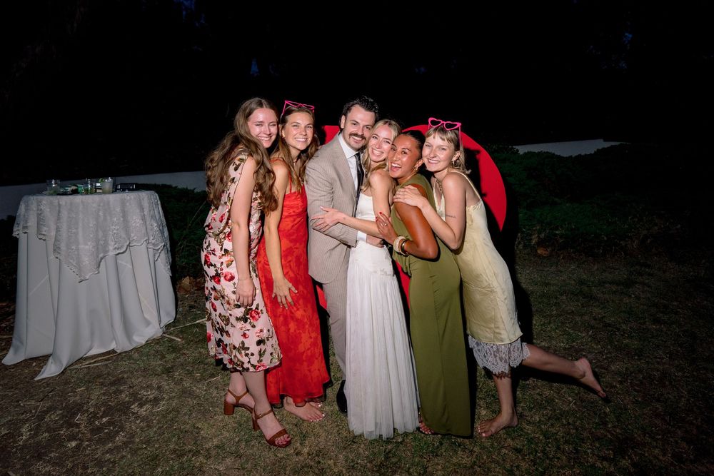 Bride and groom pose with smiling wedding guests outdoors at a nighttime reception celebration.