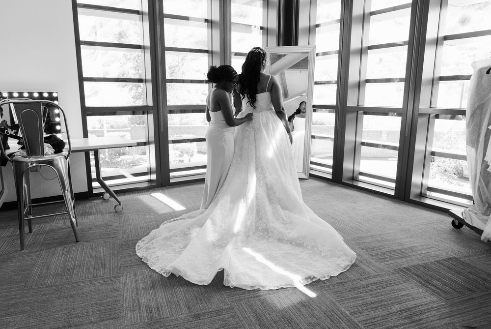 Bride and bridesmaid share tender moment in black and white photo with wedding dress train spread out.