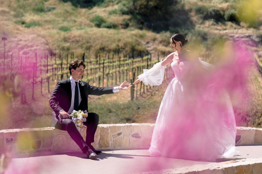 Bride and groom share romantic moment on stone terrace surrounded by pink blooms.