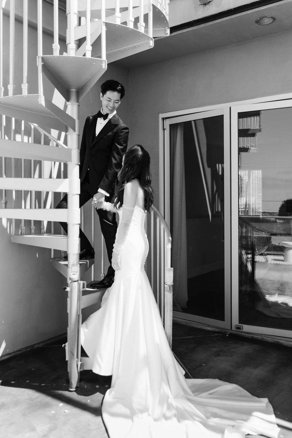 Black and white photo of bride and groom sharing a moment by a spiral staircase.