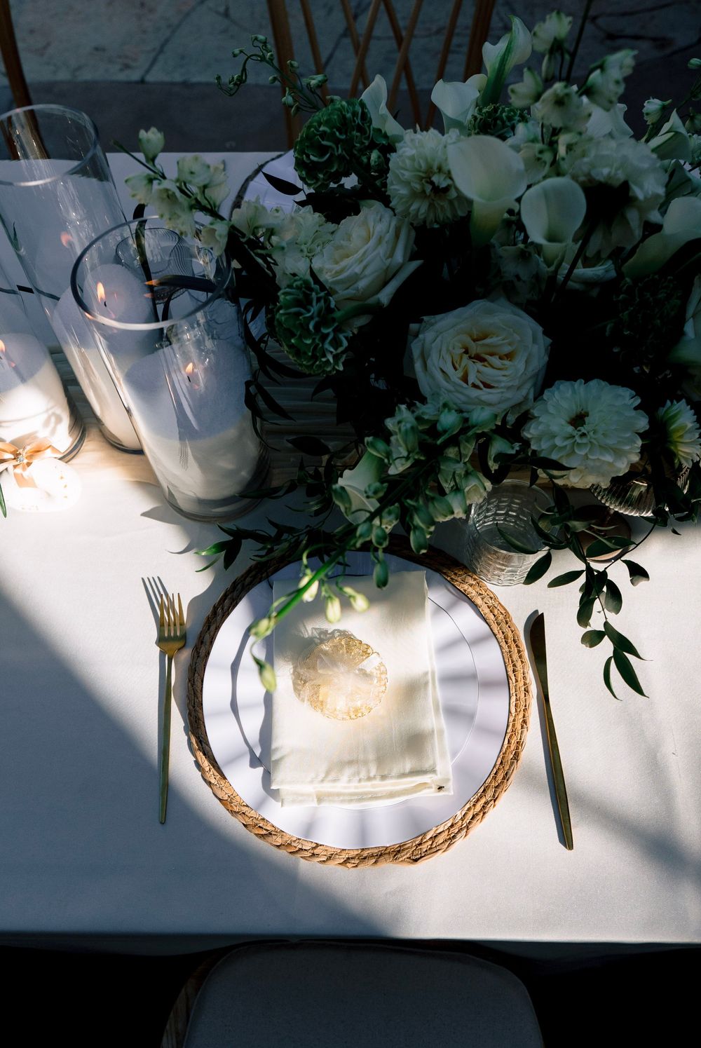 Elegant wedding table setting with gold charger, brass flatware, white florals, and candlelight centerpiece.