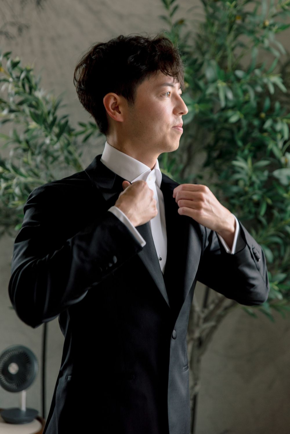 Groom in black tuxedo adjusting his collar while getting ready before the wedding ceremony.