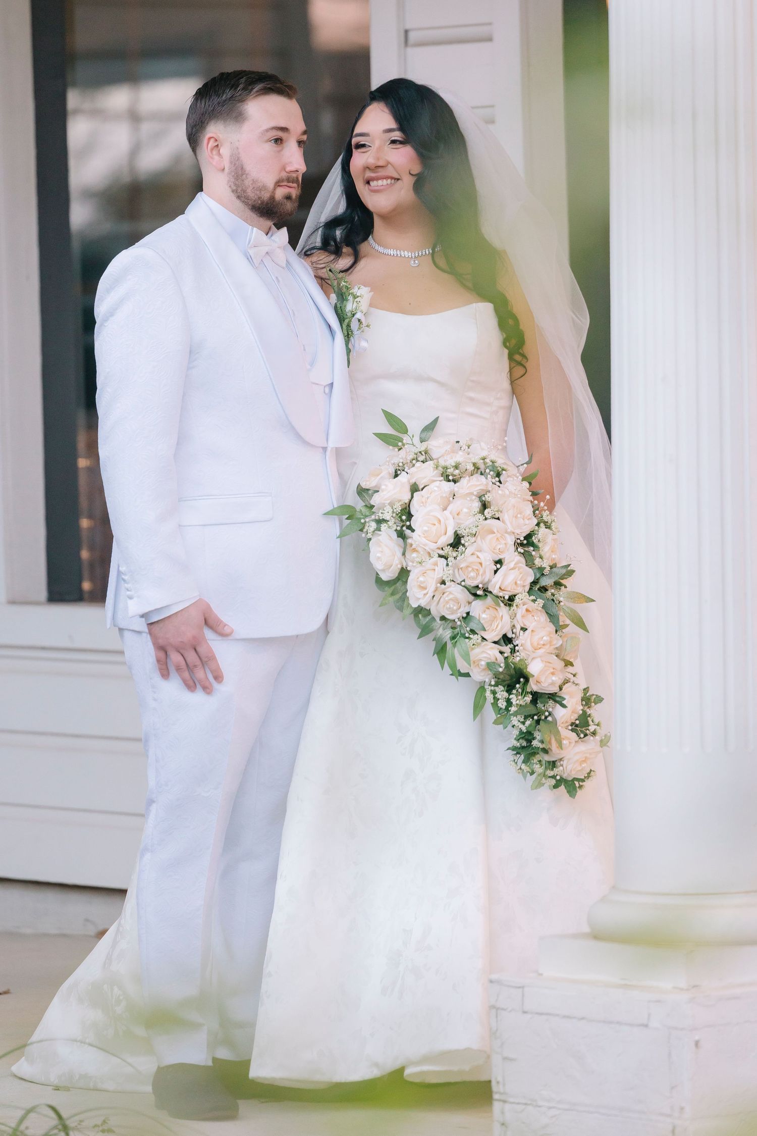 Wedding couple in matching white and beige attire pose together by a scenic pond on their special day.