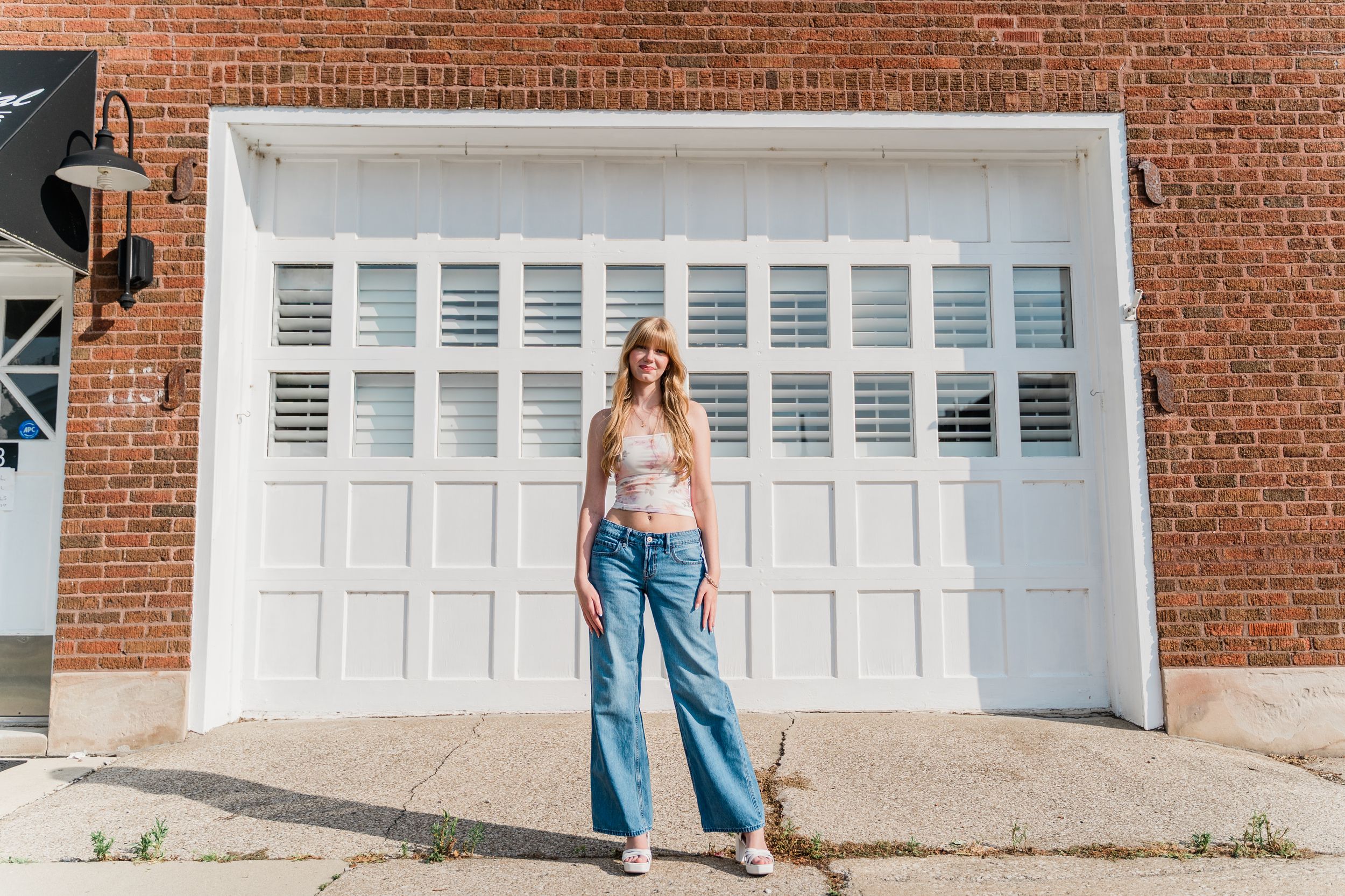 A casual summer outfit worn against a white garage door and brick wall backdrop in urban setting.