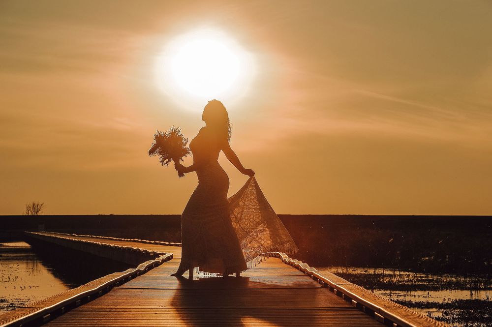 Romantic silhouette of bride at sunset against golden sky.