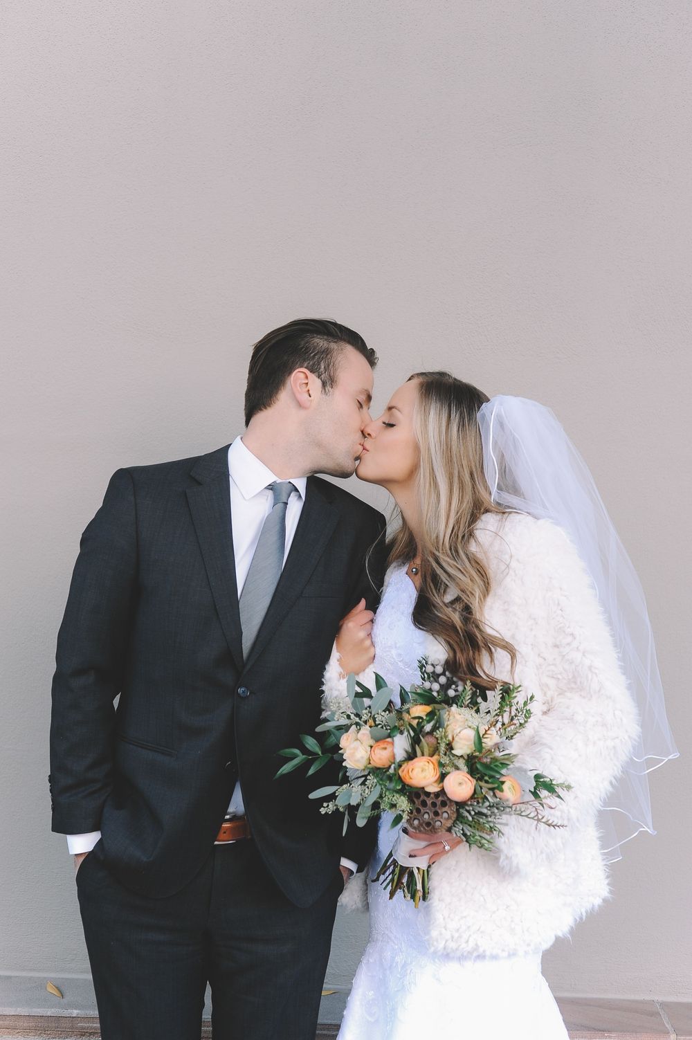 Elegant wedding couple sharing intimate moment in formal attire against neutral background.