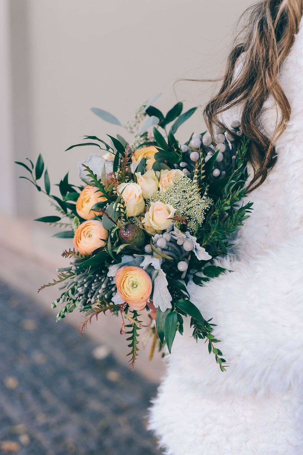 Beautiful bridal bouquet featuring peach ranunculus and greenery against white lace.
