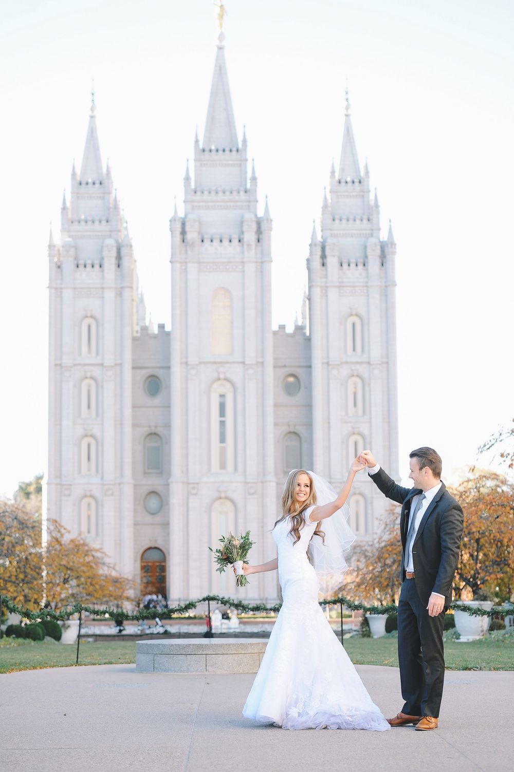 Wedding couple celebrating in front of historic Salt Lake Temple with joyful expressions.