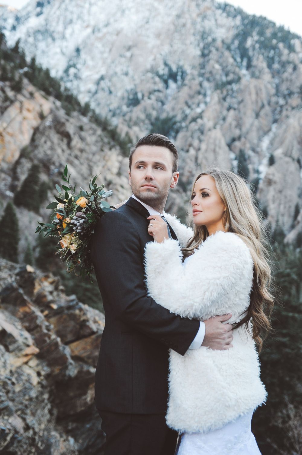 Couple embraces against dramatic mountain cliffs during winter photo session.