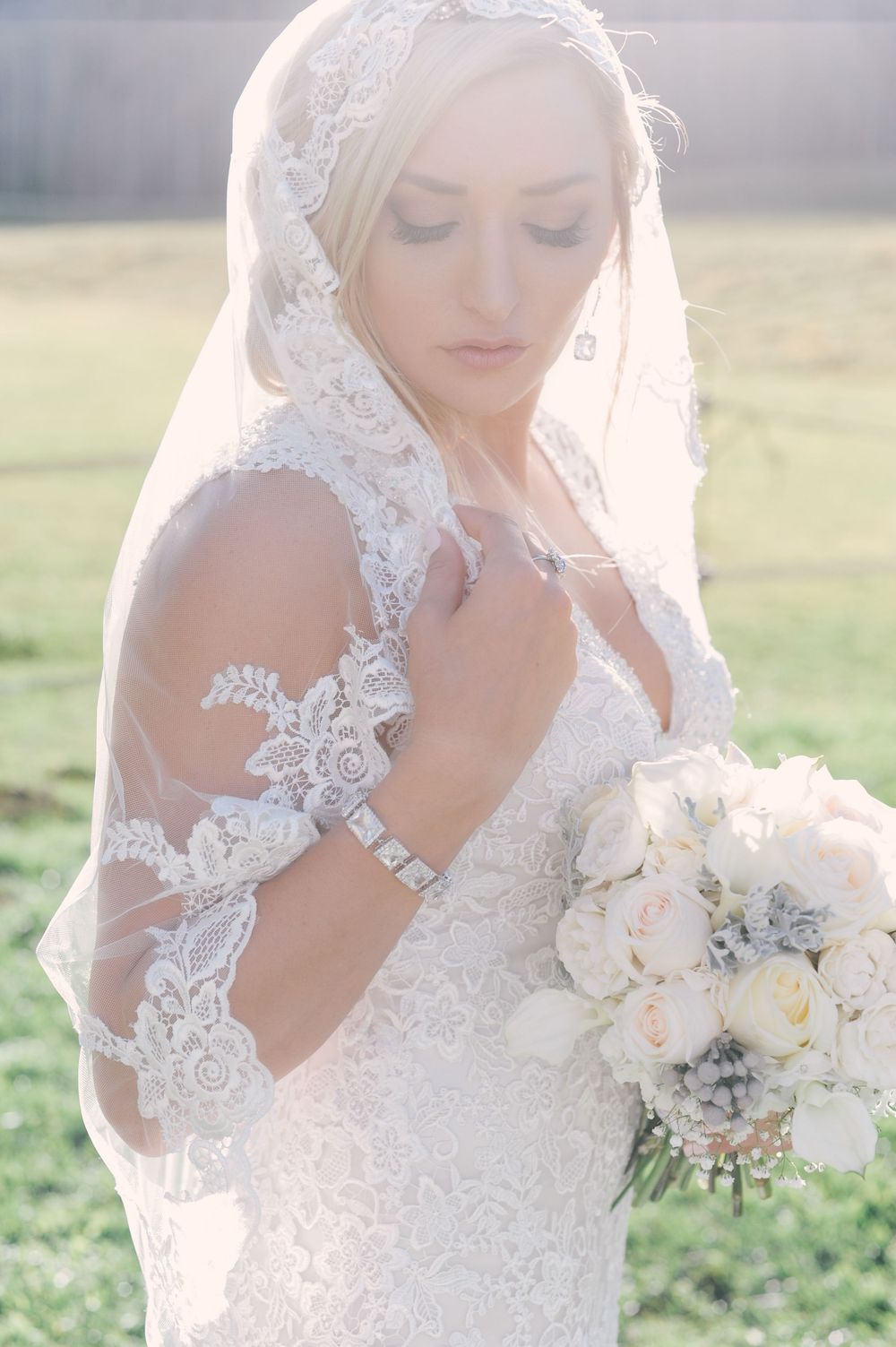 Close-up of bride holding delicate white and silver bouquet with lace dress details.